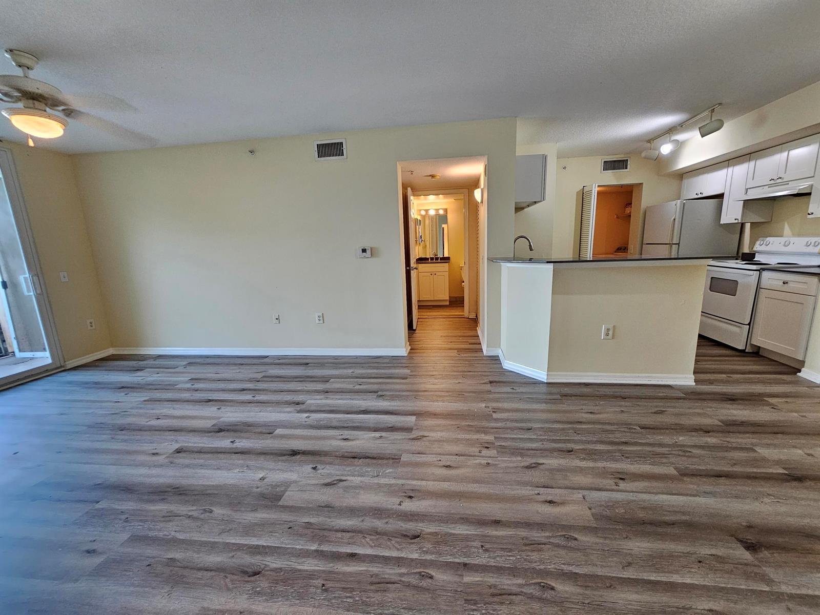 An open-concept living area features wood-look flooring, a kitchen with white cabinets, and a hallway — 604 Villa Circle # 604, Boynton Beach FL 33435, BOYNTON BEACH, FL