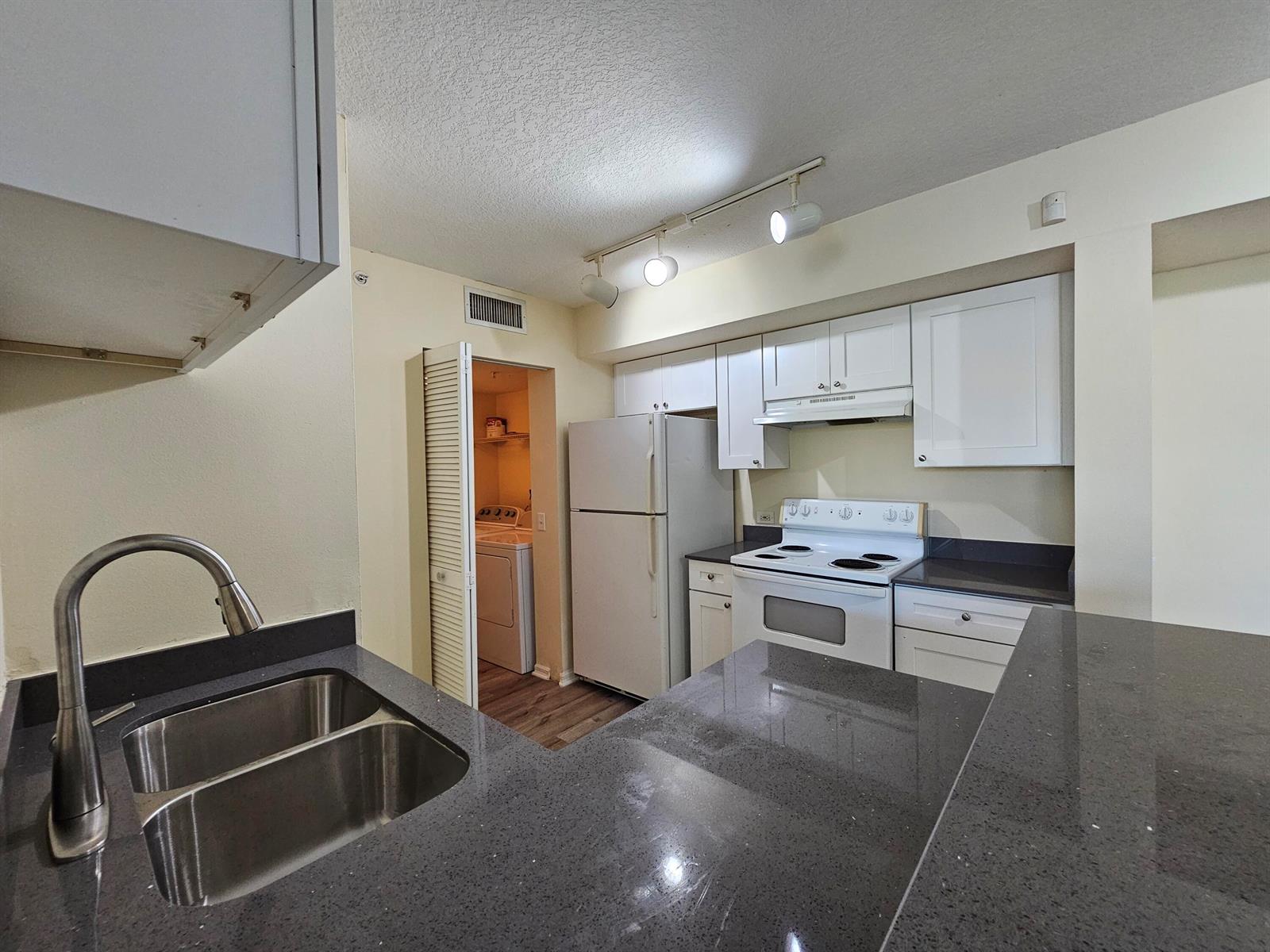 A kitchen features white cabinets, dark countertops, a double sink, and an adjacent laundry closet — 604 Villa Circle # 604, Boynton Beach FL 33435, BOYNTON BEACH, FL