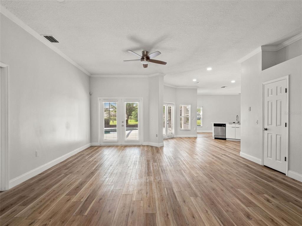 An open-concept living area features light wood-look flooring, white walls, and a ceiling fan — 5809 GUENEVERE COURT, ST CLOUD, FL