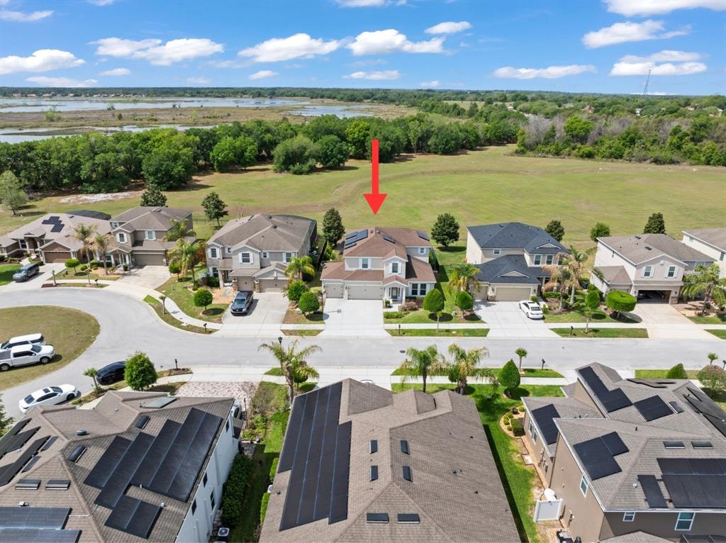 An aerial view shows a suburban neighborhood with houses, solar panels, and a grassy field — 635 NEPTUNE DRIVE, GROVELAND, FL