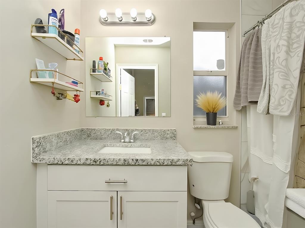 A bathroom features a granite-topped vanity, white cabinets, wall-mounted shelves, a mirror, and a toilet — 7047 HICKORY BRANCH CIRCLE, ORLANDO, FL