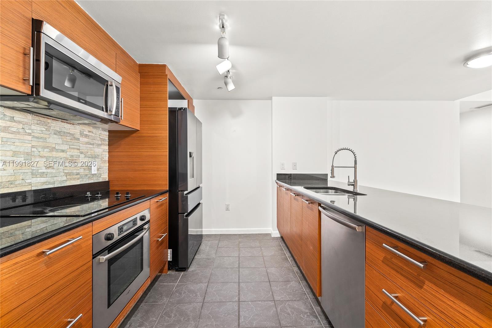 A galley kitchen features wood-grain cabinets, black countertops, stainless steel appliances, and tiled flooring — 50 Biscayne Blvd # 4111, Miami FL 33132, MIAMI, FL