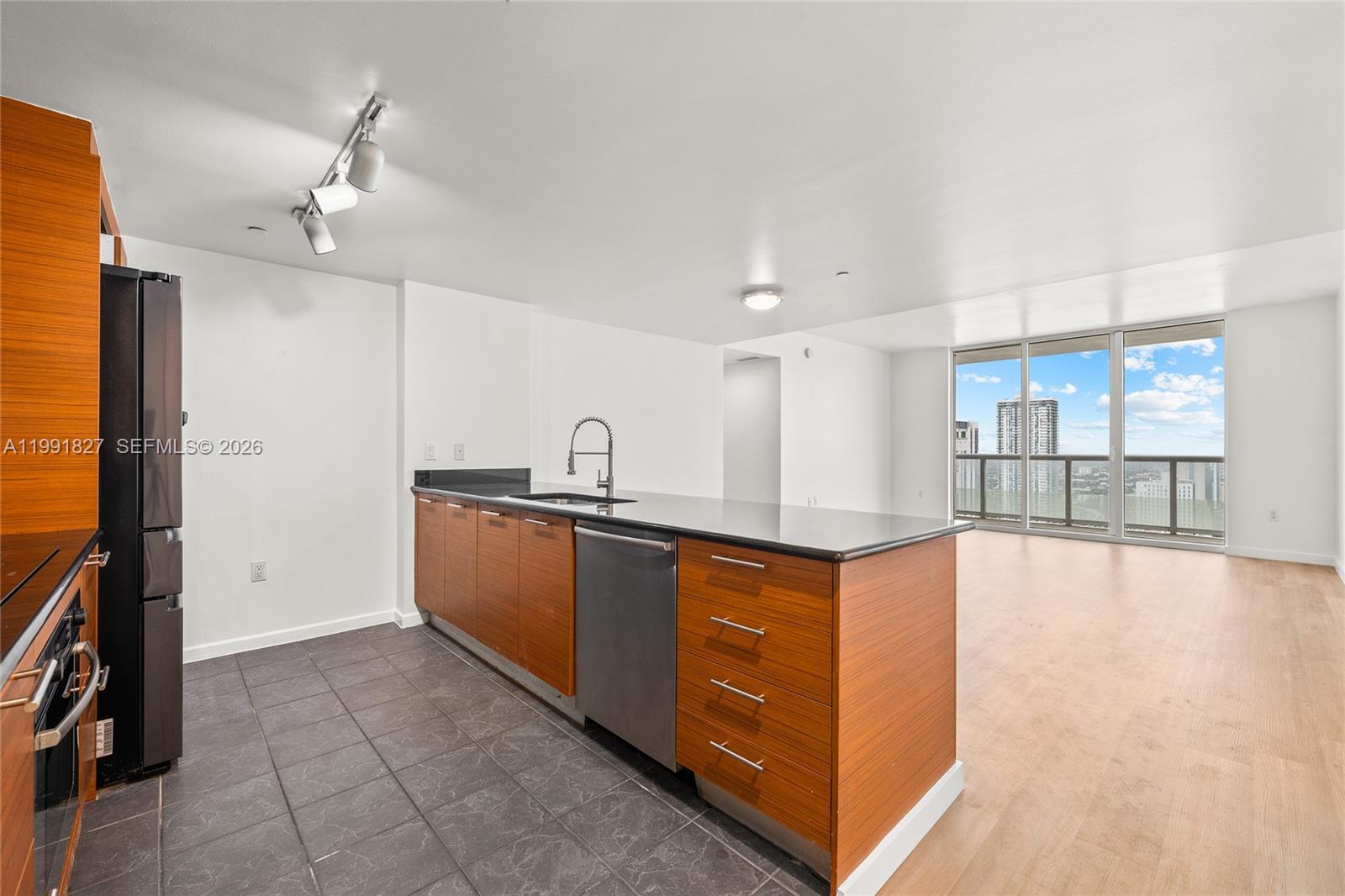A kitchen with wood cabinets, dark countertops, and tile flooring opens to a living area — 50 Biscayne Blvd # 4111, Miami FL 33132, MIAMI, FL