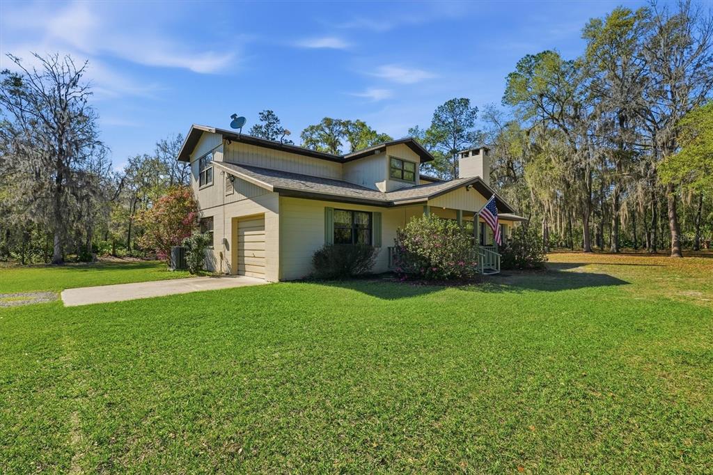 A two-story house with tan siding, a garage, and an American flag on the porch — 14600 NW 216TH PLACE, MICANOPY, FL
