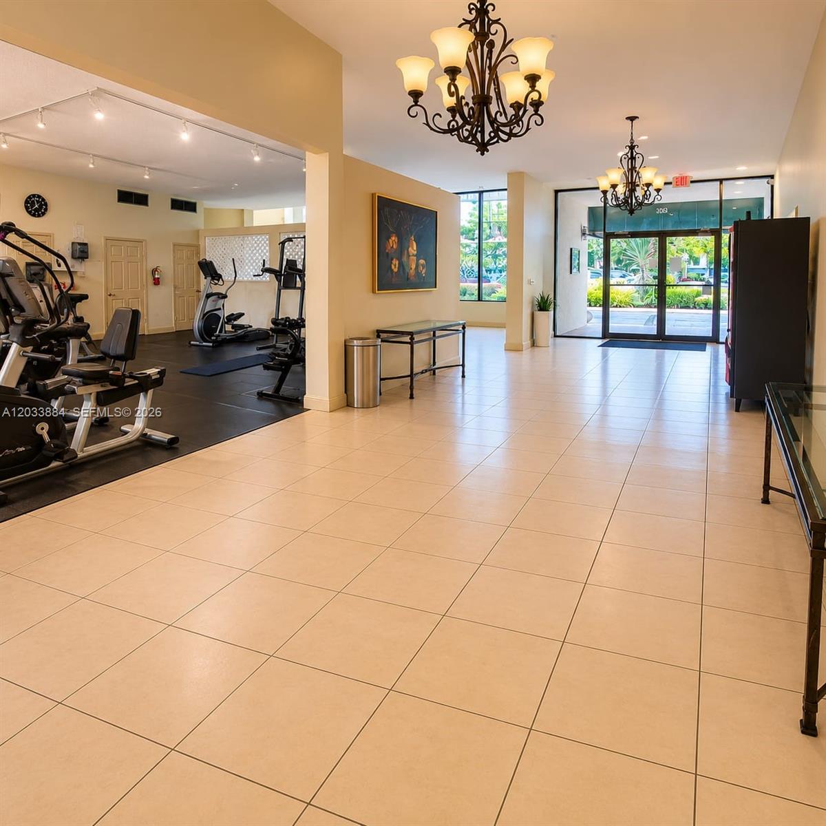 This room features a fitness area with gym equipment, tiled flooring, and two ornate chandeliers — 800 Parkview Dr # 512, Hallandale Beach FL 33009, HALLANDALE BEACH, FL