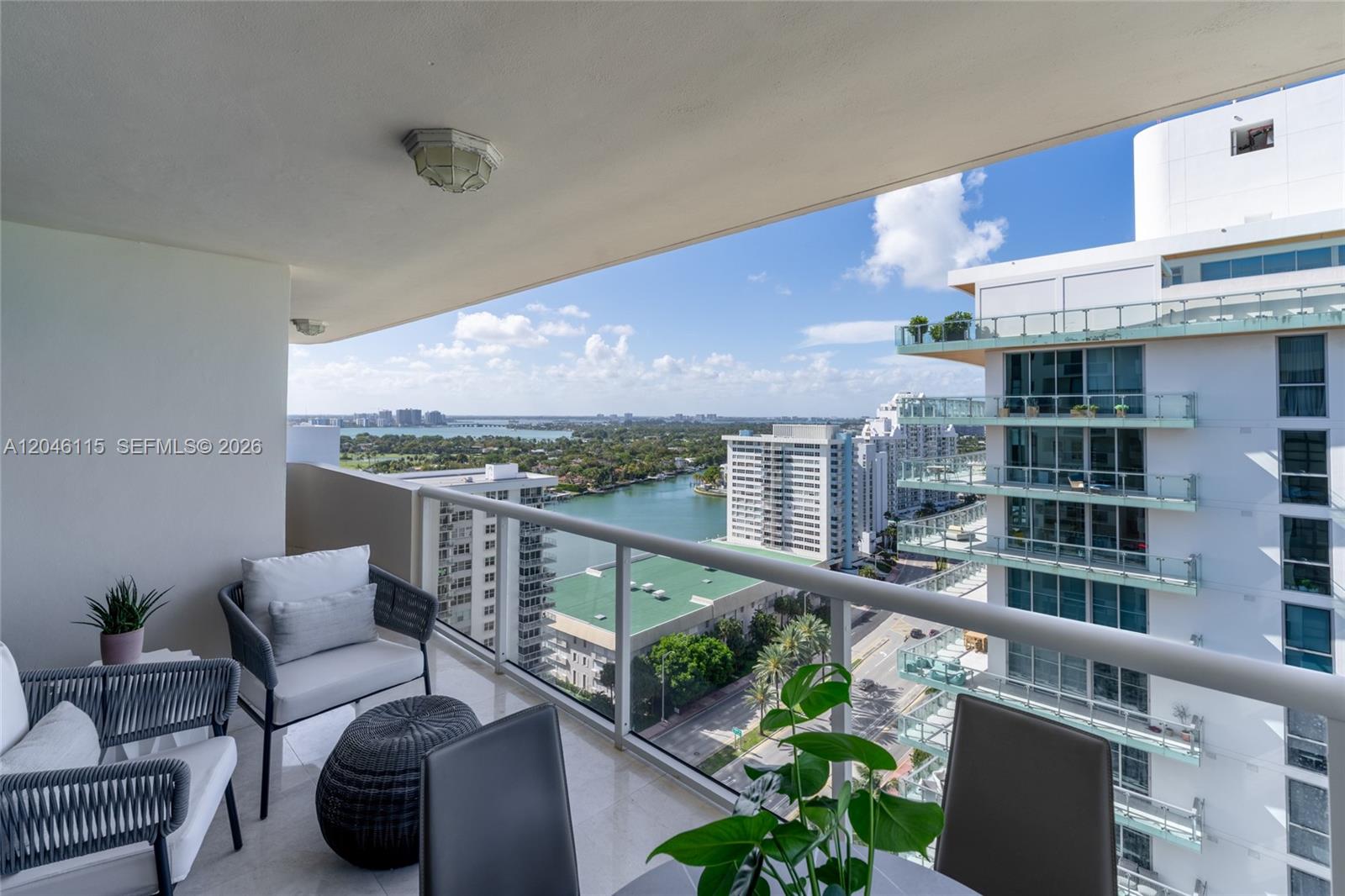 A balcony with outdoor furniture overlooks a city skyline, a waterway, and nearby high-rise buildings — 5757 Collins Ave # 2207, Miami Beach FL 33140, MIAMI BEACH, FL