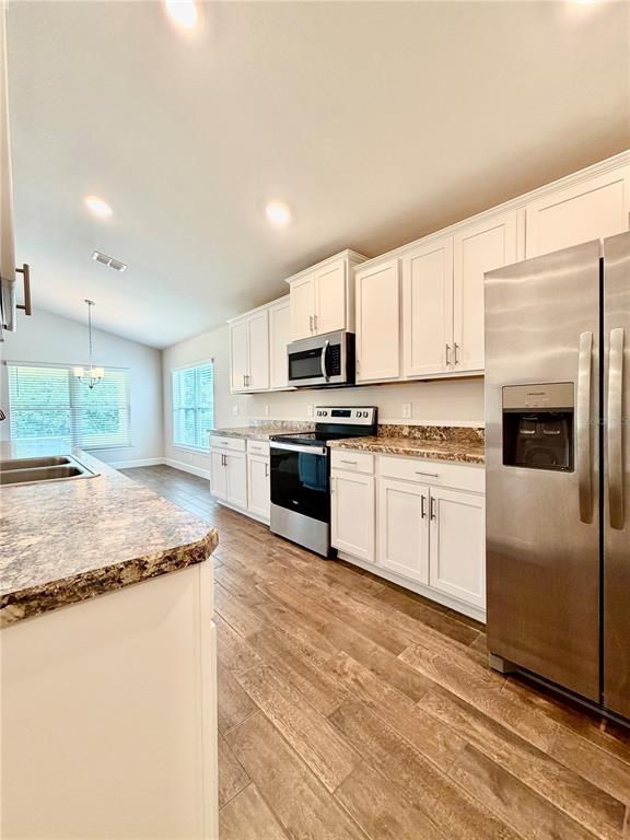 A kitchen features white cabinets, granite countertops, stainless steel appliances, and wood-look tile flooring — 633 W REXFORD DRIVE, BEVERLY HILLS, FL