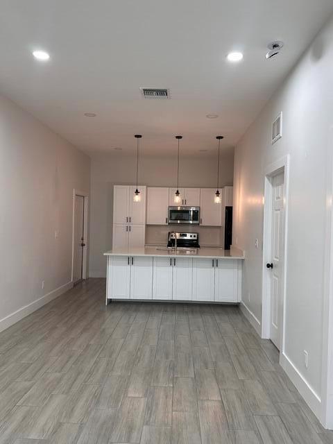 A modern kitchen features white cabinetry, stainless steel appliances, and gray wood-look tile flooring — 651 NE 60th Avenue, Okeechobee FL 34974, OKEECHOBEE, FL