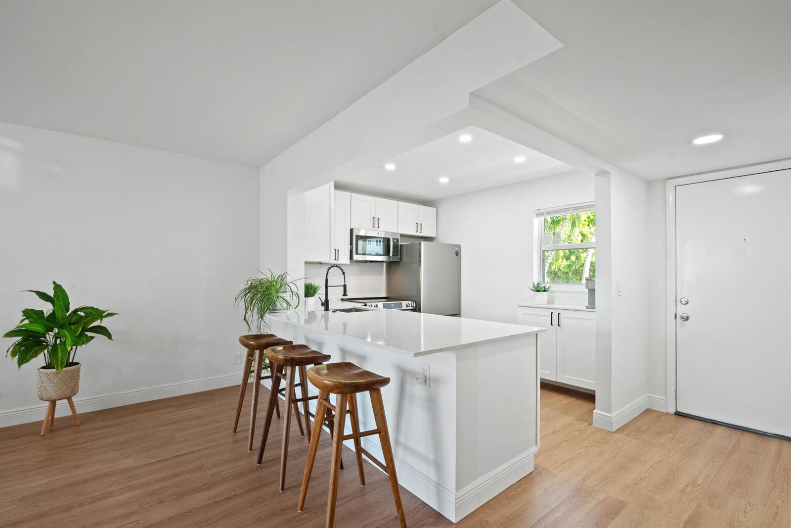 A kitchen with a white breakfast bar, three wooden stools, and light wood flooring — 230 NE 26th Avenue # 2160, Boynton Beach FL 33435, BOYNTON BEACH, FL