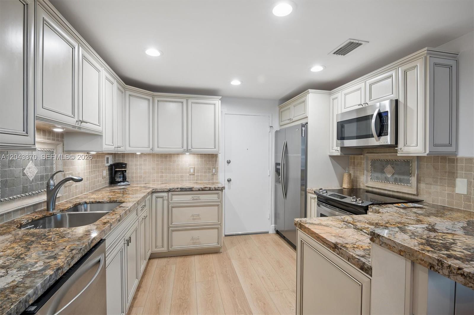 A kitchen features light-colored cabinets, granite countertops, stainless steel appliances, and wood-look flooring — 3505 S Ocean Dr # 708, Hollywood FL 33019, HOLLYWOOD, FL