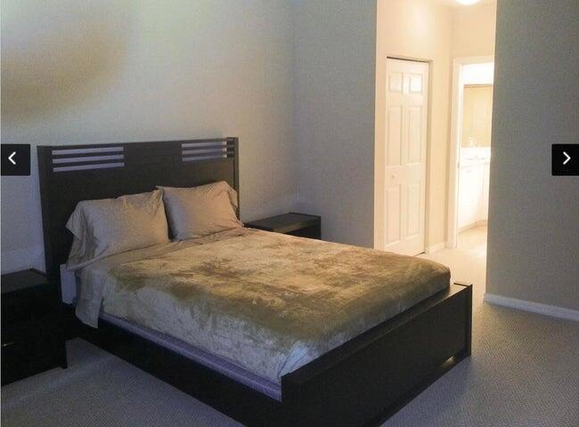 A bedroom features a dark wood platform bed with a tan comforter and carpeted flooring — 804 E Windward Way # 119, Lantana FL 33462, LANTANA, FL