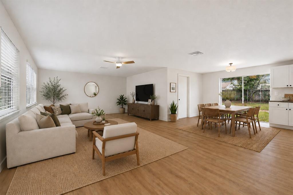 An open-concept living and dining area features light wood flooring, neutral walls, and large windows — 9001 ARNDALE CIRCLE, TAMPA, FL