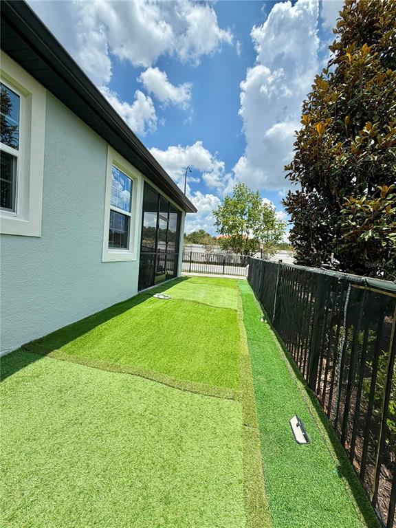 A side yard features artificial turf, a black metal fence, and a house exterior — 7963 BOYDEN WAY, KISSIMMEE, FL
