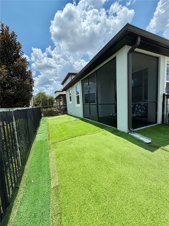 A backyard with artificial turf, a black metal fence, and a screened-in patio — 7963 BOYDEN WAY, KISSIMMEE, FL