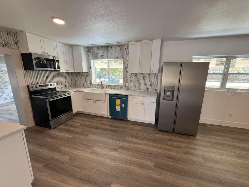 A kitchen features white cabinets, stainless steel appliances, a farmhouse sink, and wood-look flooring — 4217 WD JUDGE DRIVE UNIT W, ORLANDO, FL