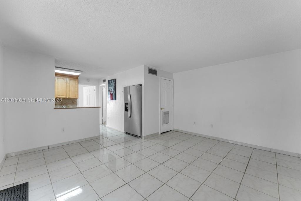 A room with white walls, white tile flooring, a stainless steel refrigerator, and kitchen cabinetry — 10832 N Kendall Dr # U1, Miami FL 33176, MIAMI, FL