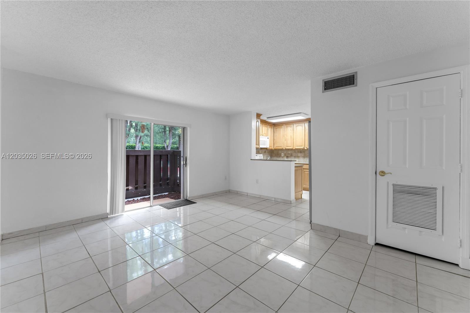 A living room with white tile floors leads to a kitchen and a sliding glass door — 10832 N Kendall Dr # U1, Miami FL 33176, MIAMI, FL