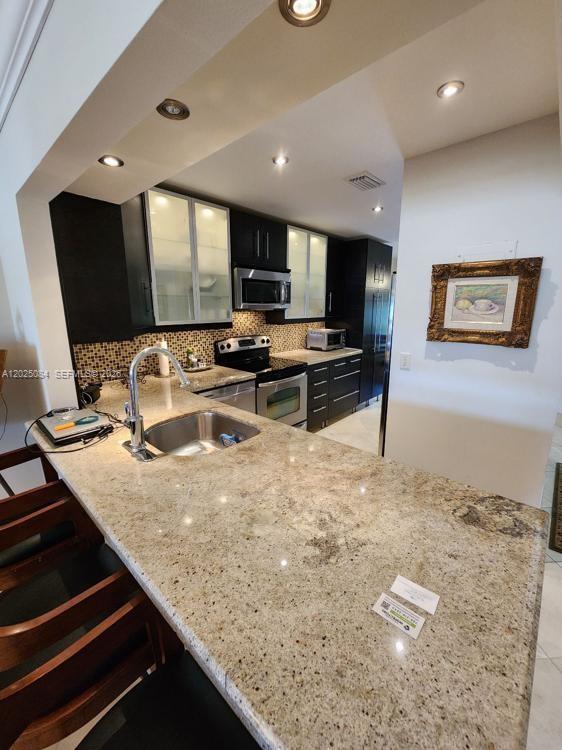 A kitchen features granite countertops, dark cabinetry, stainless steel appliances, and a breakfast bar — 5590 Via Delray # B, Delray Beach FL 33484, DELRAY BEACH, FL