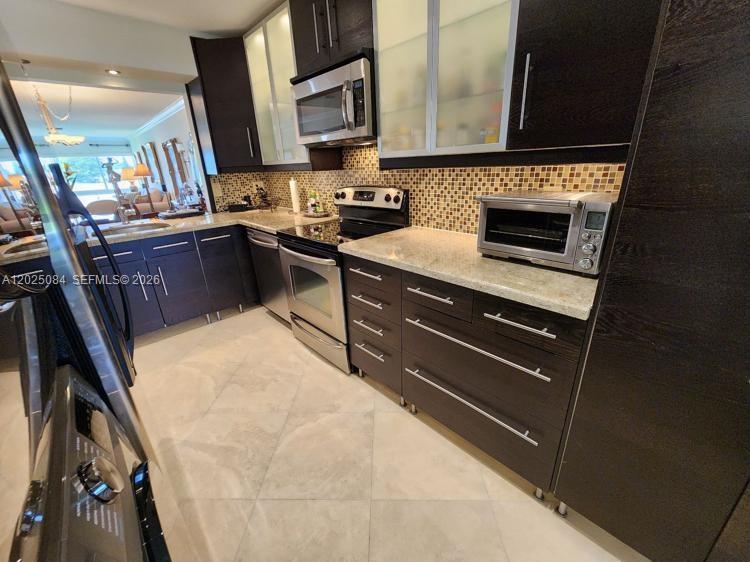 A kitchen features dark wood cabinets, granite countertops, a tiled backsplash, and stainless steel appliances — 5590 Via Delray # B, Delray Beach FL 33484, DELRAY BEACH, FL