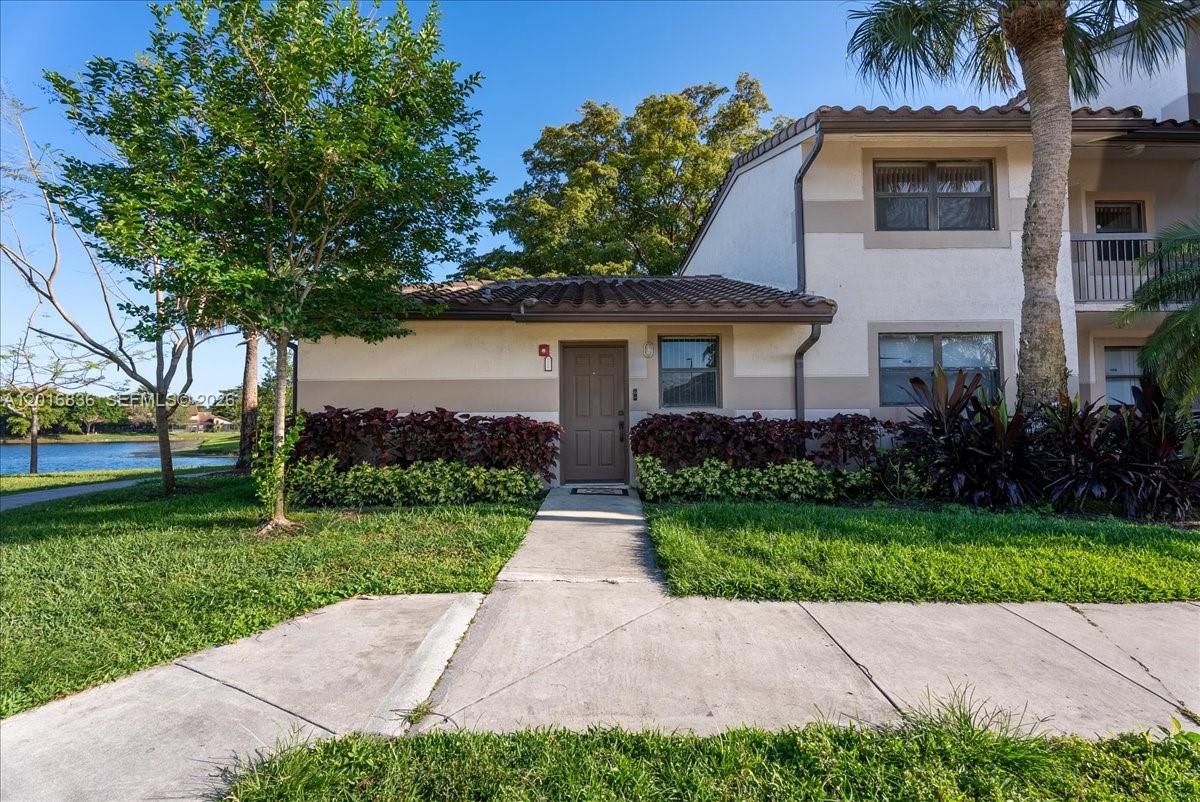 A tan, one-story residential building with a brown door and tile roof near a lake — 9860 Nob Hill Ln # 9860, Sunrise FL 33351, SUNRISE, FL