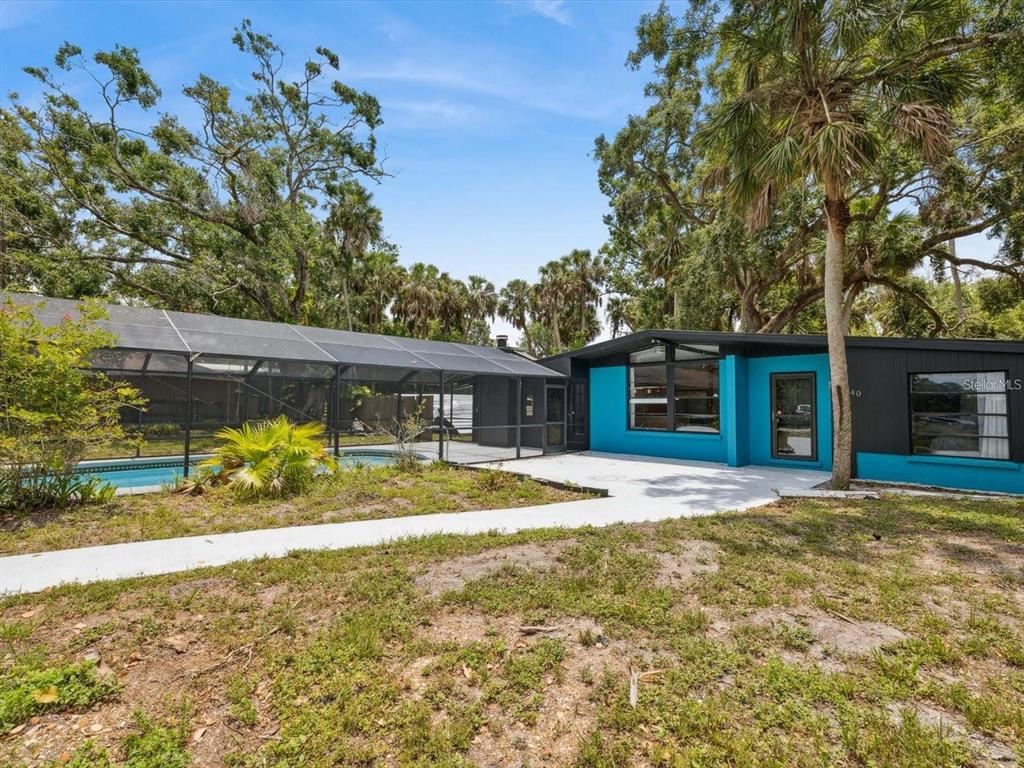 A house with a turquoise accent wall, a screened pool enclosure, and surrounding mature trees — 6440 RICHARDSON ROAD, SARASOTA, FL