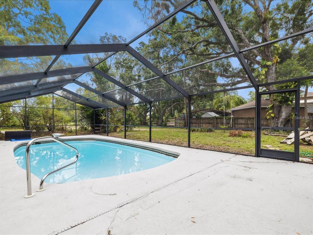 A swimming pool is enclosed by a screened lanai with a concrete deck and backyard view — 6440 RICHARDSON ROAD, SARASOTA, FL