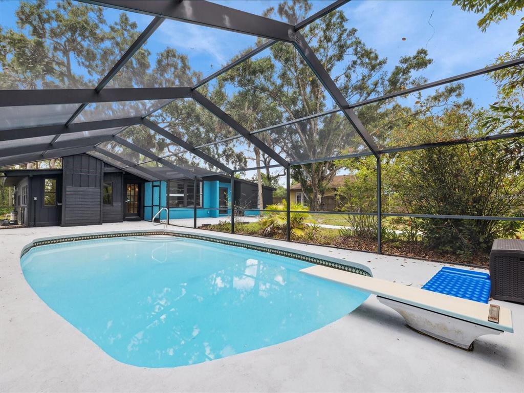 A swimming pool with a diving board is enclosed by a screened lanai behind a house — 6440 RICHARDSON ROAD, SARASOTA, FL