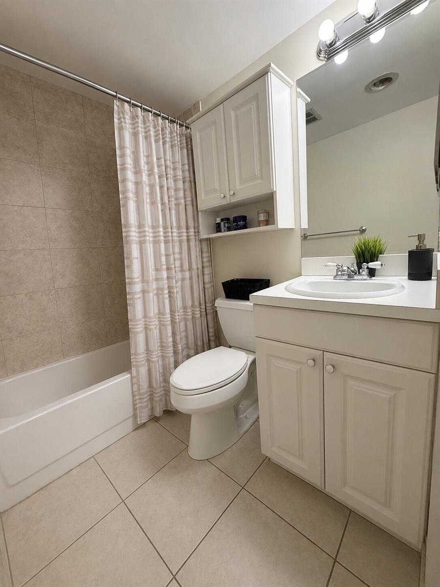A bathroom featuring a white vanity, a toilet, and a shower-tub combo with beige tiles — 4168 INVERRARY Drive # 103, Lauderhill FL 33319, LAUDERHILL, FL