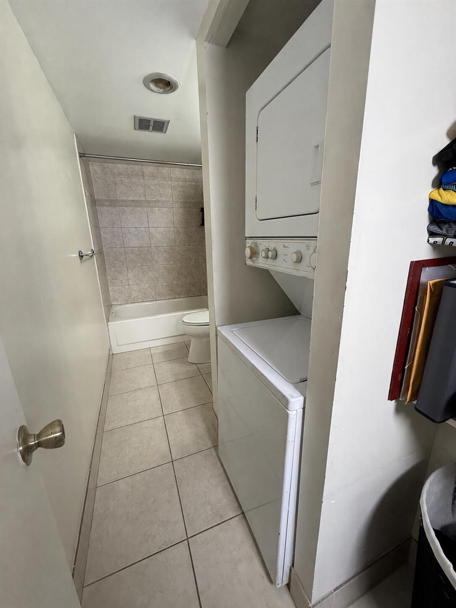 A bathroom with a tiled floor and tub, featuring a stacked washer and dryer unit — 4168 INVERRARY Drive # 103, Lauderhill FL 33319, LAUDERHILL, FL