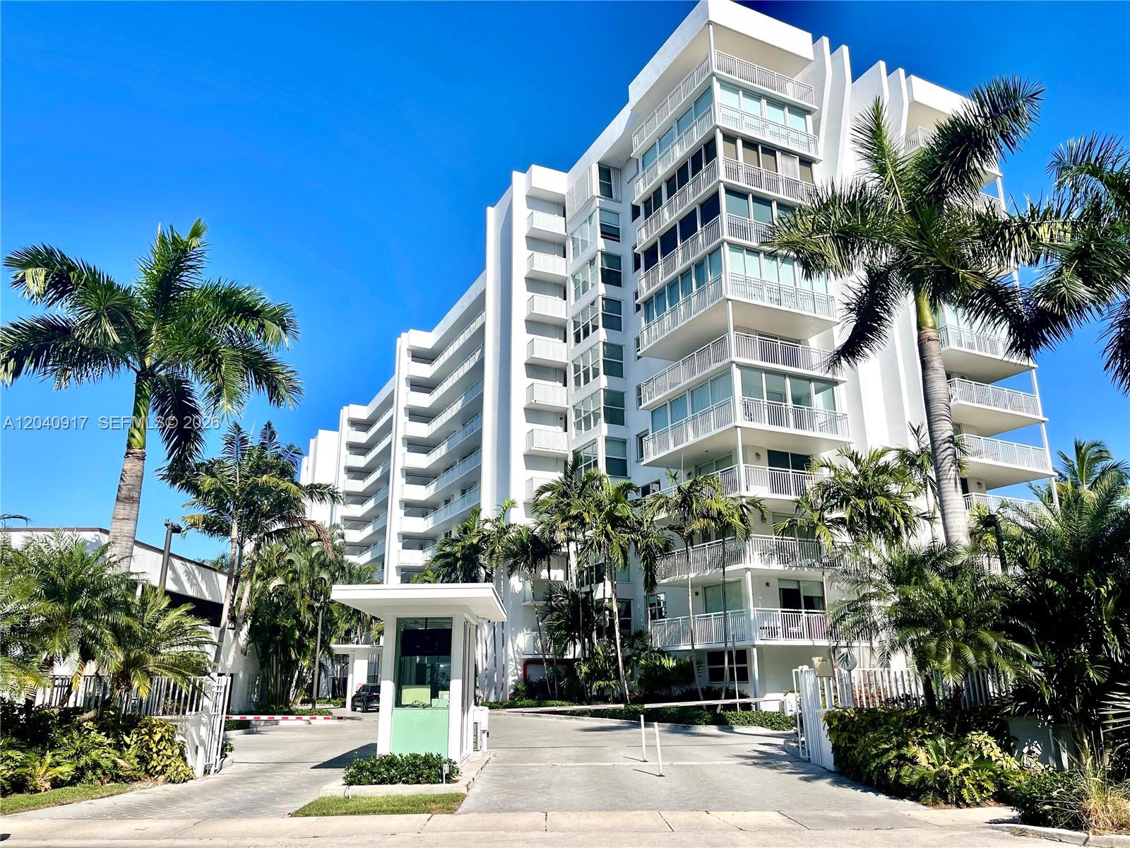 A white multi-story residential building features balconies and palm trees at a gated entrance — 607 Ocean Dr # 3K, Key Biscayne FL 33149, KEY BISCAYNE, FL