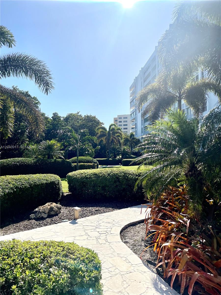 A stone path winds through a landscaped garden with palm trees and a residential building — 607 Ocean Dr # 3K, Key Biscayne FL 33149, KEY BISCAYNE, FL