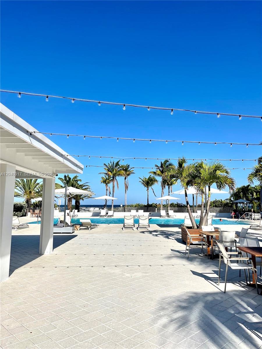 A patio with outdoor seating overlooks a swimming pool and palm trees under a clear sky — 607 Ocean Dr # 3K, Key Biscayne FL 33149, KEY BISCAYNE, FL