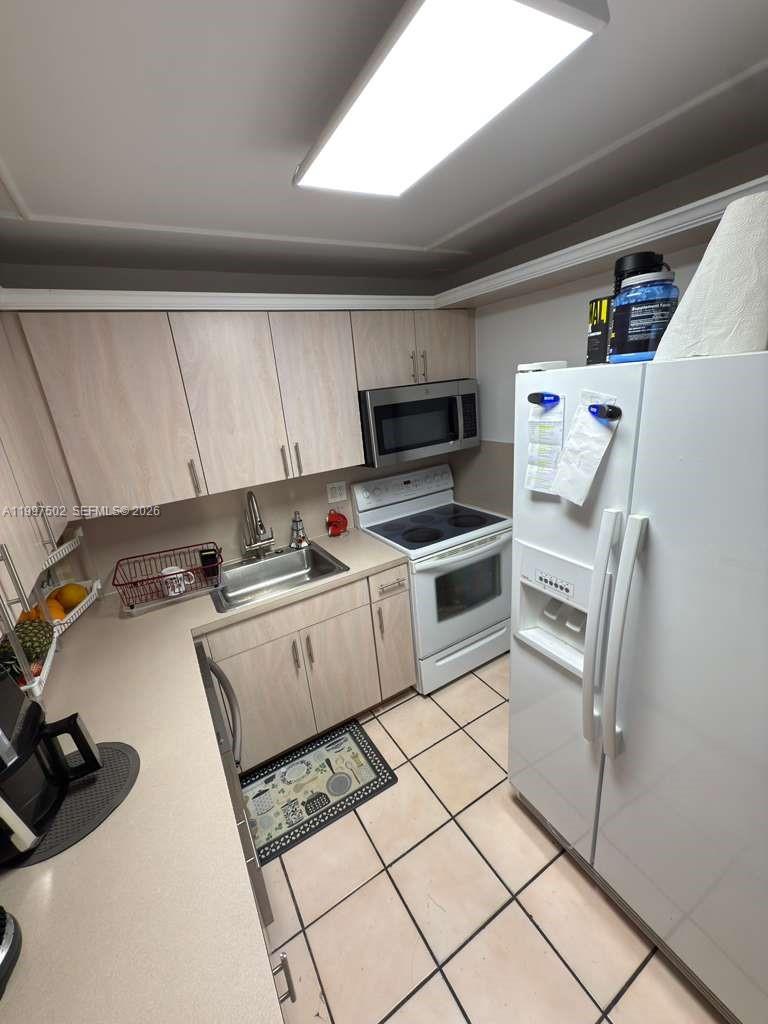 A kitchen features light wood cabinets, white appliances, a stainless steel sink, and tile flooring — 1825 W 44th Pl # 208, Hialeah FL 33012, HIALEAH, FL