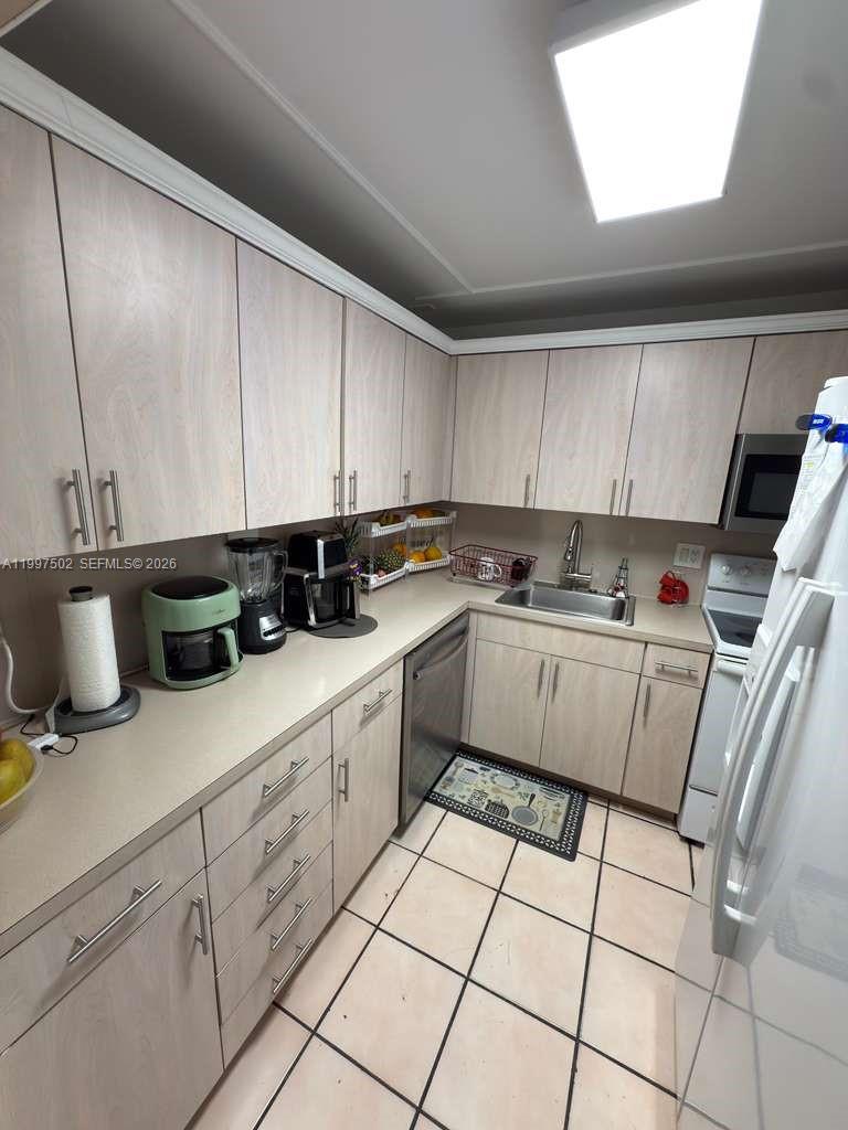 A galley kitchen features light wood-grain cabinets, beige countertops, and white tile flooring — 1825 W 44th Pl # 208, Hialeah FL 33012, HIALEAH, FL