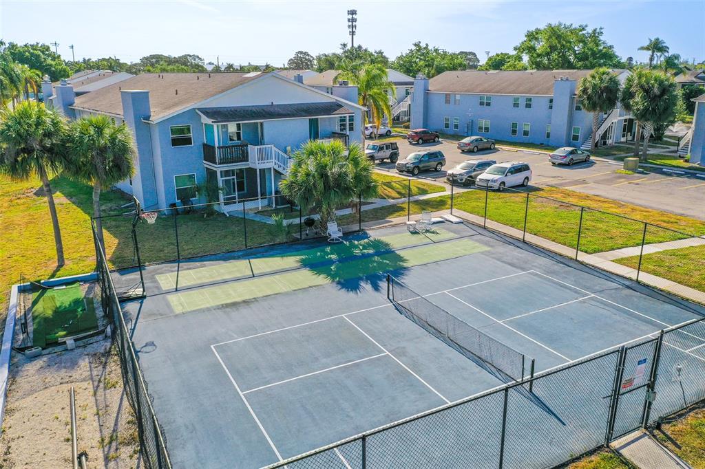 An aerial view of a fenced tennis court next to a blue multi-story apartment building — 3784 59TH AVENUE W UNIT 3784, BRADENTON, FL