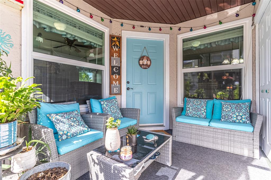 A covered porch features wicker furniture with blue cushions, a glass coffee table, and a door — 3784 59TH AVENUE W UNIT 3784, BRADENTON, FL