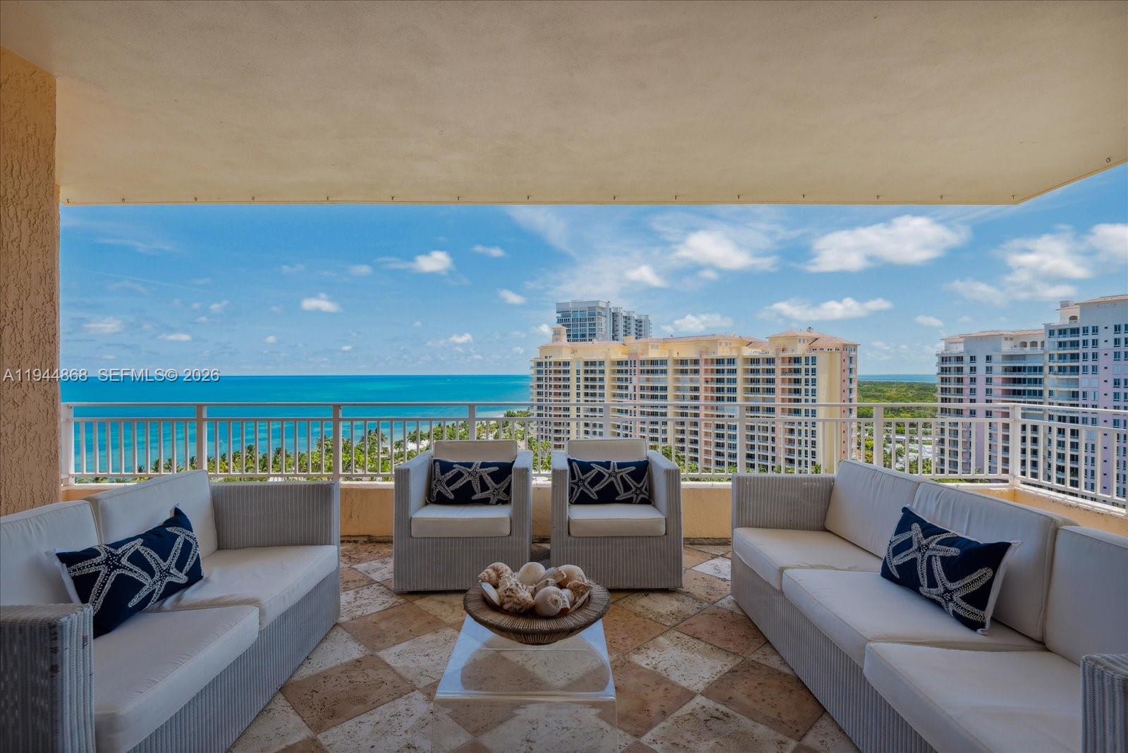 A balcony features white wicker furniture with starfish pillows, a shell centerpiece, and ocean views — 791 Crandon Blvd # 1501, Key Biscayne FL 33149, KEY BISCAYNE, FL