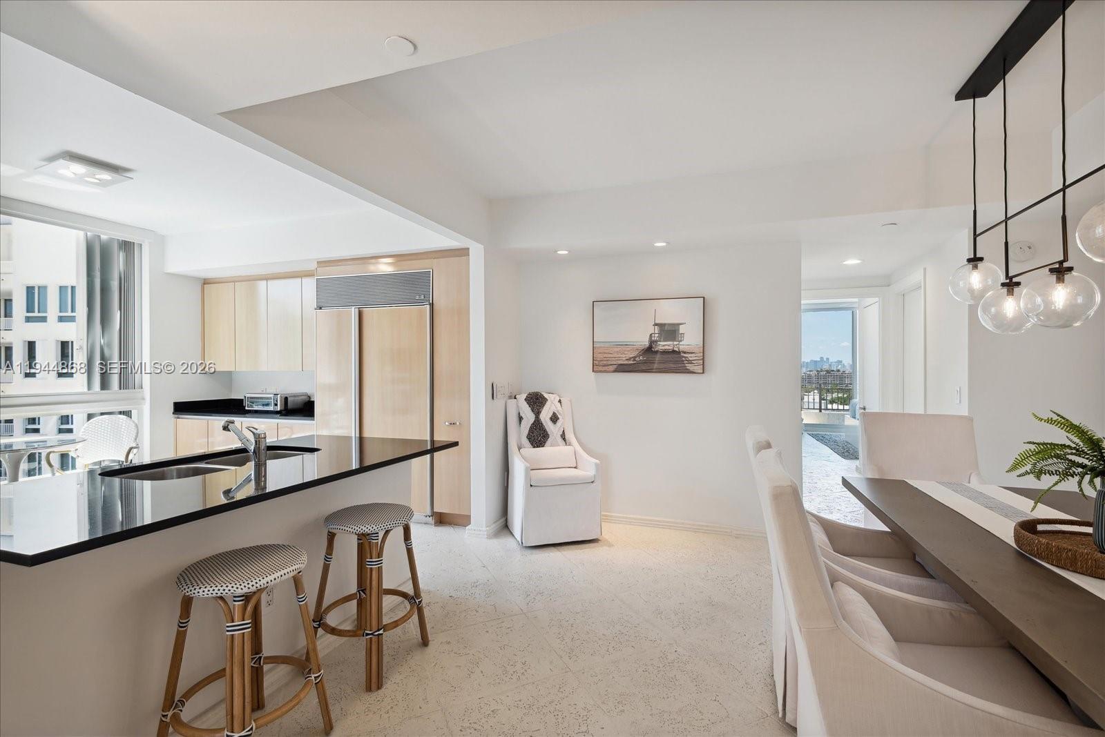 A modern kitchen with a black island and bar stools opens to a dining area — 791 Crandon Blvd # 1501, Key Biscayne FL 33149, KEY BISCAYNE, FL