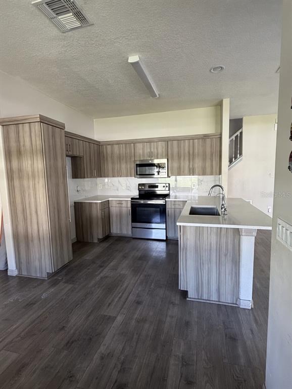 A kitchen features light wood-grain cabinets, stainless steel appliances, a center island, and dark flooring — 14114 ABACO ISLE DRIVE, ORLANDO, FL