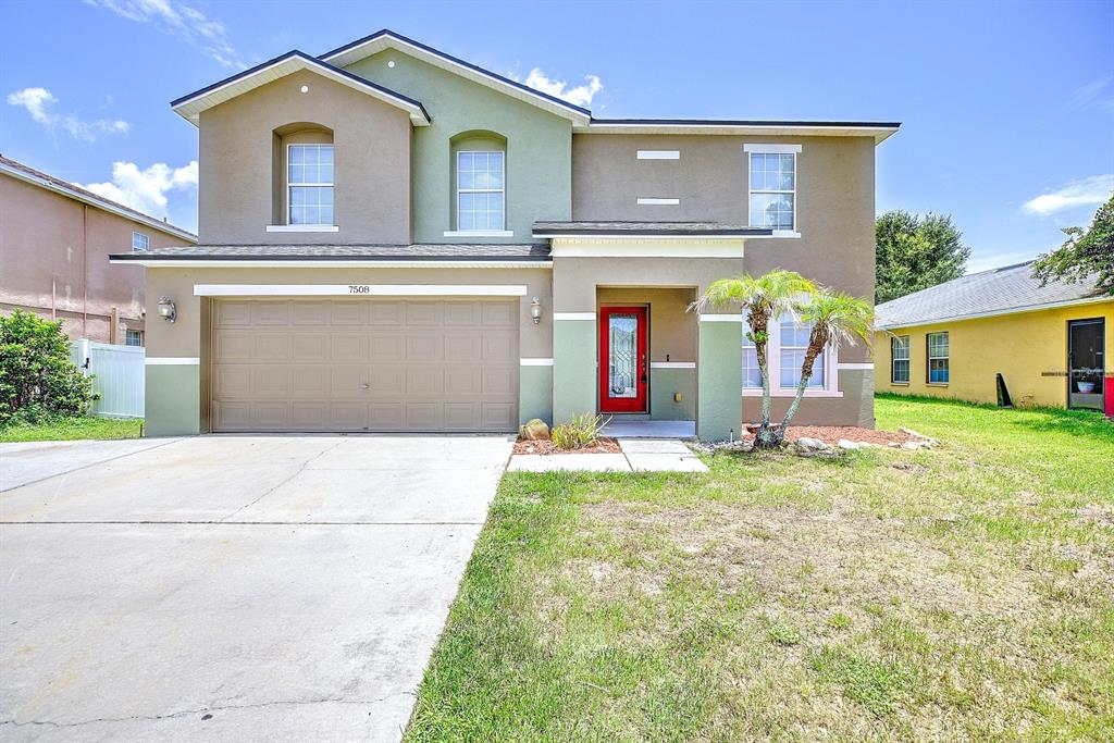 A two-story house with a tan and green exterior, a two-car garage, and a red door — 7508 HUNTERS GREENE CIRCLE, LAKELAND, FL