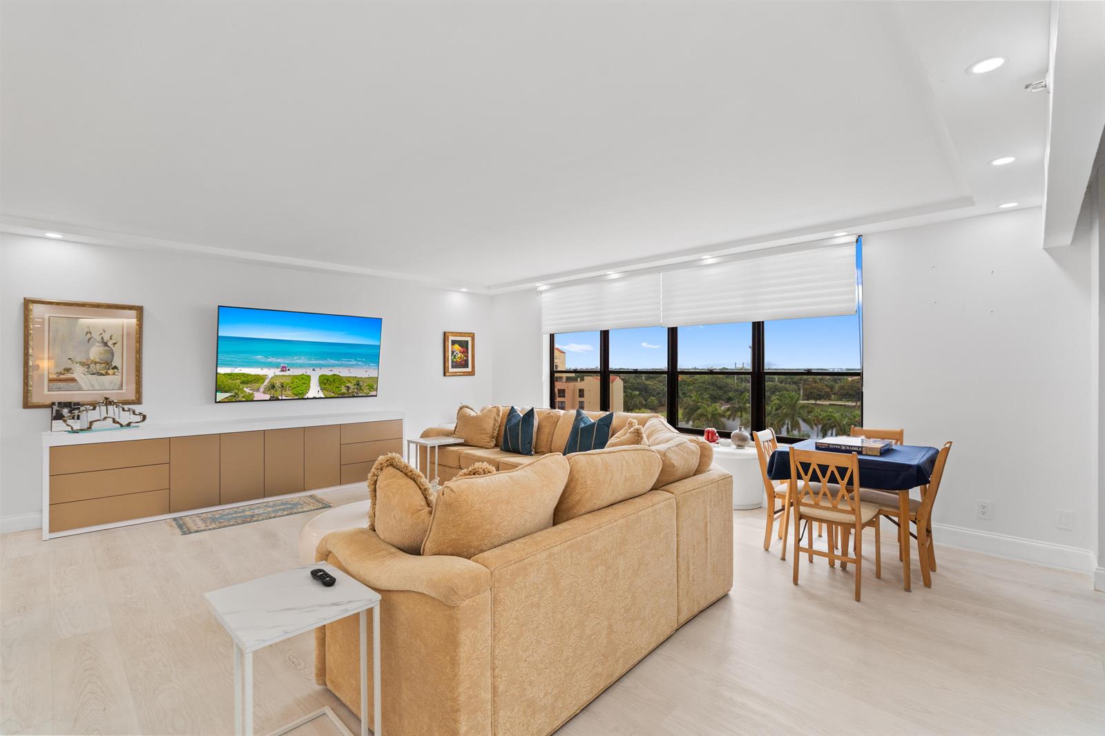 A bright living room features a large sectional sofa, a wall-mounted television, and dining area — 7209 Promenade Drive # 802, Boca Raton FL 33433, BOCA RATON, FL