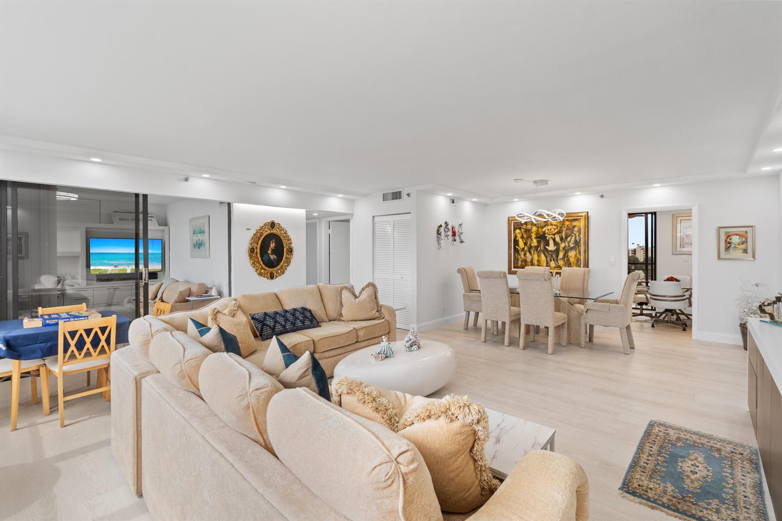 An open-concept living and dining area features light wood flooring, neutral furniture, and wall art — 7209 Promenade Drive # 802, Boca Raton FL 33433, BOCA RATON, FL