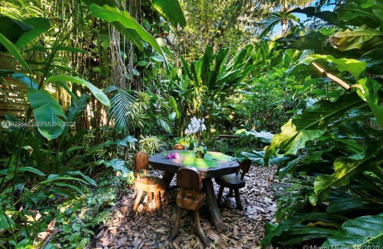 A rustic wooden table and chairs sit in a lush, tropical garden setting — 4895 SW 88th St # 00, Miami FL 33156, MIAMI, FL