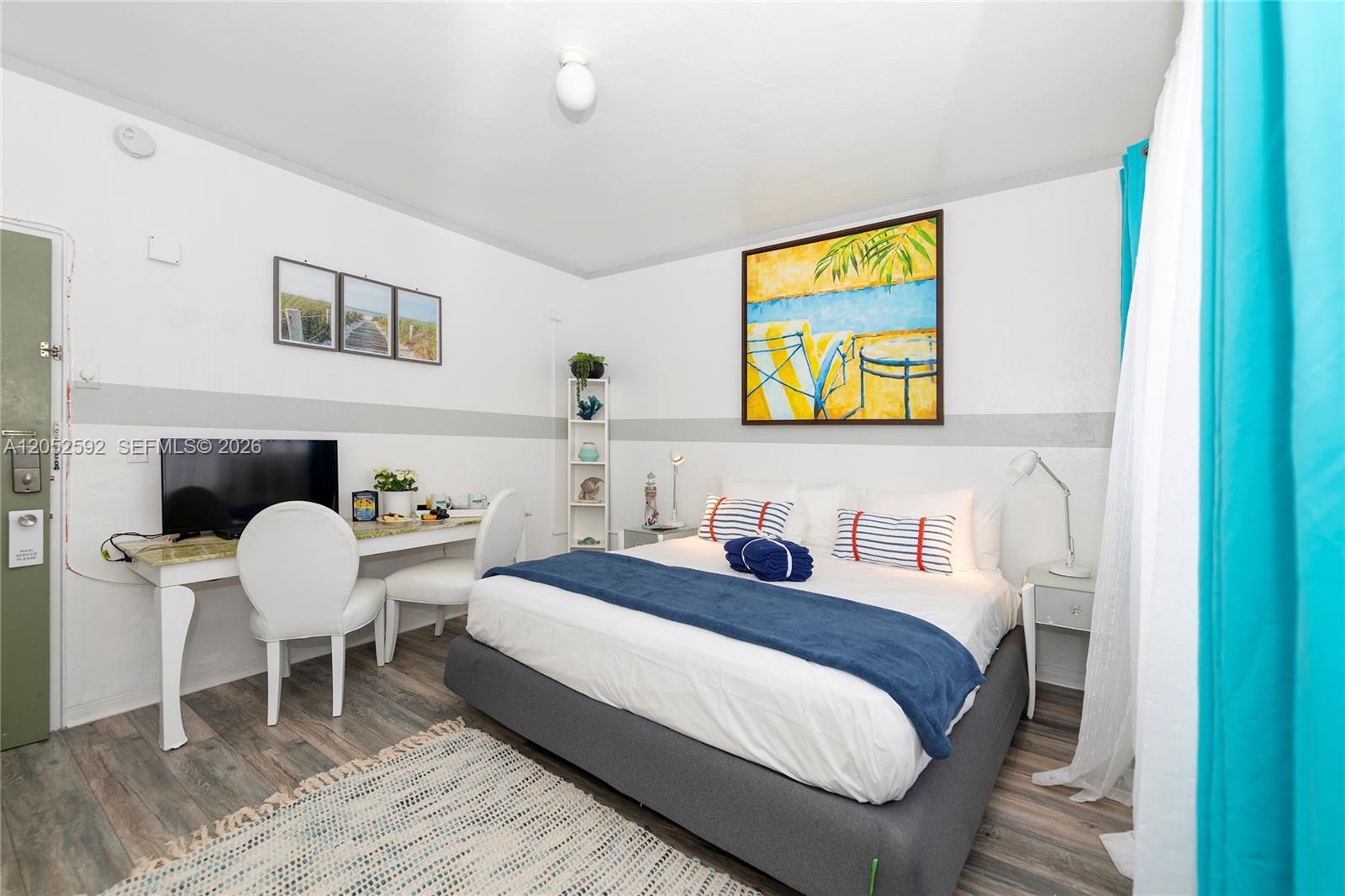 A bedroom features a bed, a desk with two chairs, and coastal-themed wall art — 6760 Collins Ave # 29, Miami Beach FL 33141, MIAMI BEACH, FL