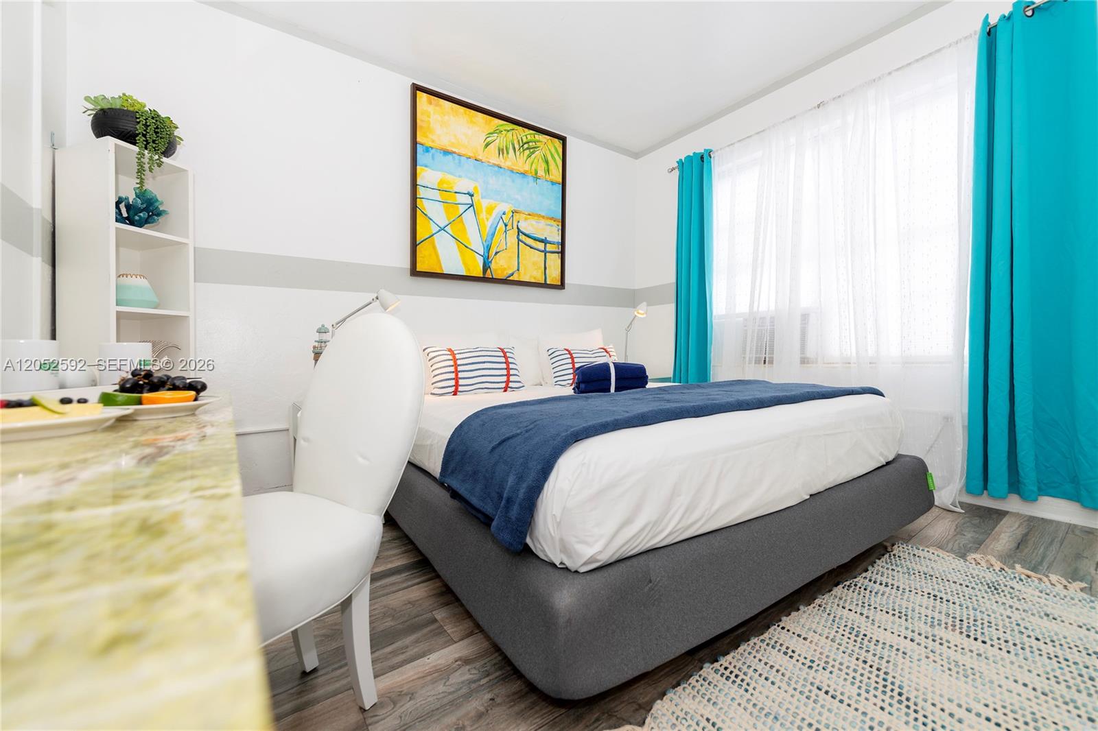A bedroom features a bed with a blue throw, a white chair, and turquoise curtains — 6760 Collins Ave # 29, Miami Beach FL 33141, MIAMI BEACH, FL