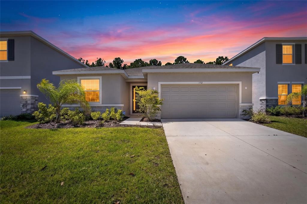 A single-story suburban house with a concrete driveway, two-car garage, and a sunset sky — 152 BRIGHT IBIS AVENUE, APOLLO BEACH, FL