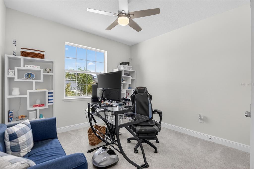 A home office features a glass desk, gaming chair, blue sofa, and white shelving units — 152 BRIGHT IBIS AVENUE, APOLLO BEACH, FL
