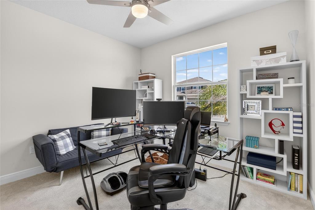 A home office features a glass desk, gaming chair, sofa, and white shelving against a window — 152 BRIGHT IBIS AVENUE, APOLLO BEACH, FL