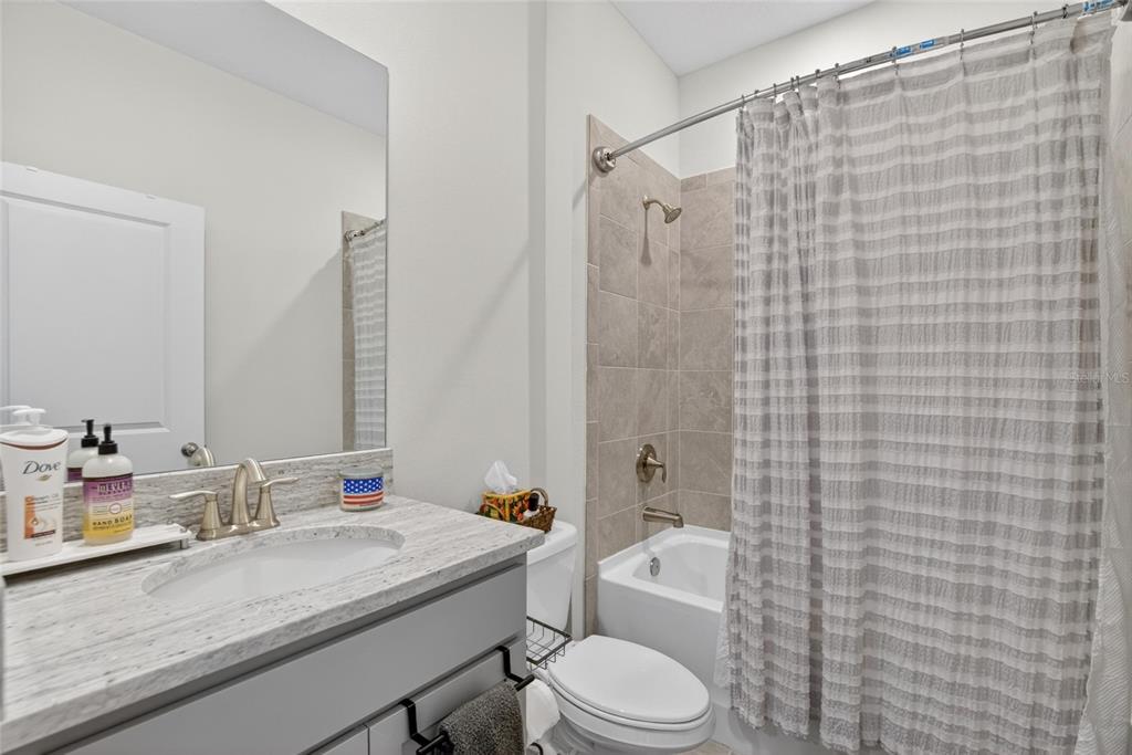 A bathroom features a vanity with a stone countertop, a mirror, and a shower-tub combo — 152 BRIGHT IBIS AVENUE, APOLLO BEACH, FL