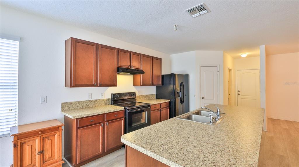 A kitchen features wood cabinets, granite countertops, a kitchen island, and black appliances — 346 ADMIRALTY COURT, EDGEWATER, FL